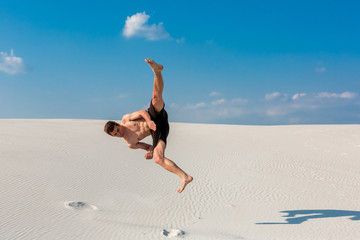 Portrait of young parkour man doing flip or somersault on the sand.