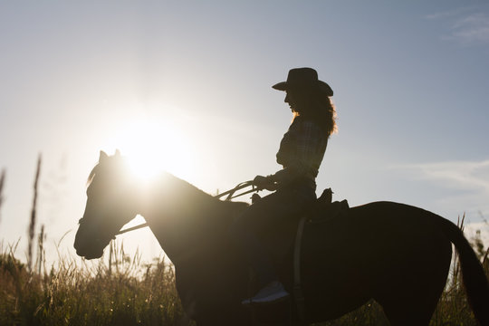 Silhouette of a woman in cowboy hat riding a horse - sunset or sunrise, horizontal