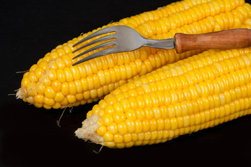 yellow fresh corn with fork on black background