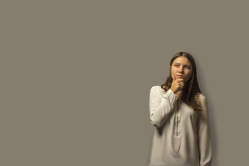 portrait of a young beautiful student girl holding her hand near her face and thinking. isolated on a gray background. the decision-making concept. a lot of copy space.