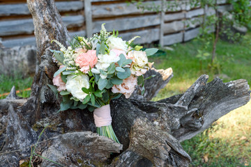 Obraz na płótnie Canvas Beautiful wedding bouquet of fresh white and pink roses and greenery standing on wood stump outdoors, free space. Close up of bridal bouquet, copy space