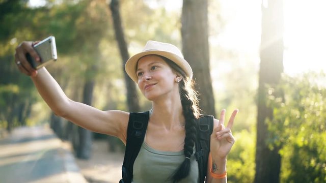 Funny tourist girl in hat taking selfie photos with smartphone camera during travelling and hitchhiking