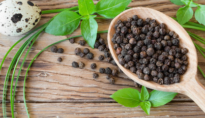 Black peppercorns in a wooden spoon on the table with basil, onion and quail egg. Pile of black...