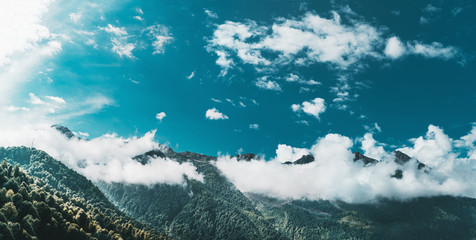 Stunning morning panoramic scenery with mountains and hills ridges covered by low clouds, teal sunny sky; environs of Krasnaya Polyana, Sochi, Ruissa, where Winter Olympic Games 2014 took place - obrazy, fototapety, plakaty