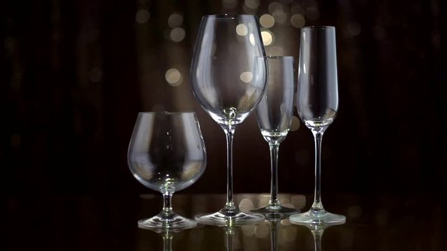 Different empty types of glasses over holiday blinking dark background. Drinkware. Slow motion 4K UHD video 3840x2160
