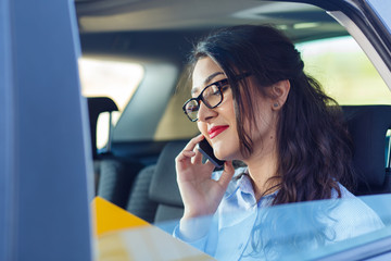 Beautiful young business woman sitting in the car looking at her planner and talking at phone.