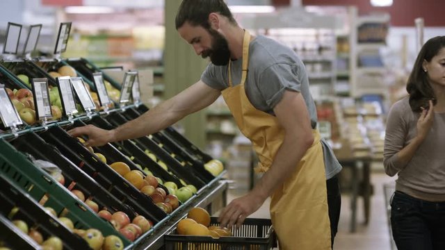  Worker stocking shelves in grocery store while customers shop