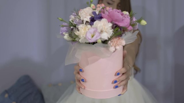 Beautiful girl presents festive box with bouquet of flowers