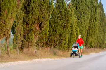 Running mother with stroller enjoying motherhood at sunset landscape