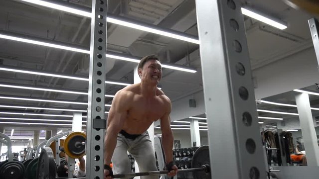 Fit shirtless man lifting barbells in gym