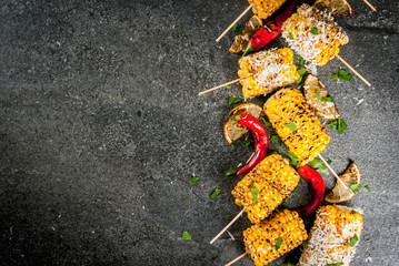Summer food. Ideas for barbecue and grill parties. Grilled corn grilled on fire. With a sprinkle of cheese (mexican elotes), hot chili pepper and lemon. On a dark stone table. Copy space top view