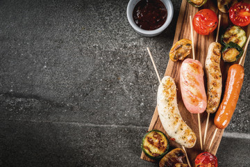 Barbecue. Assortment of various grilled meat sausages, with vegetables BBQ - mushrooms, tomatoes, zucchini, onions. On a black stone table, on cutting board plate, with sauce. Copy space top view