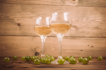 Two glasses of white wine and grapes on wooden table
