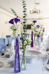 Beautiful fresh flowers on table in wedding day. Wedding table decoration. Bouquet of pink roses and purple eustoma in glass vases on dinner table in restaurant