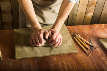 potter, workshop, ceramics art concept - closeup on male hands kneading the fireclay, a ceramist with raw material on wooden table with sculpting tool set, top view