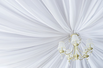 Classic chandelier hanging on ceiling made of white cloth. View from bottom.