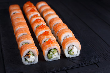 California sushi rolls set with salmon set on black slate, close up. Japanese food, sushi restaurant.