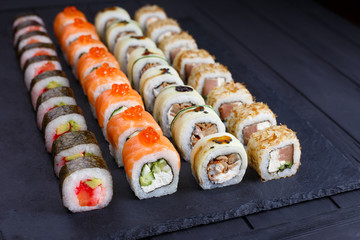 Delicious fresh multicolored sushi set on black slate, close up. Traditional japanese food, restaurant serving