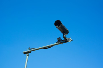 Security camera for surveillance, control, monitoring, spying and protection. Technological device is recording video. Clear blue sky in the background.