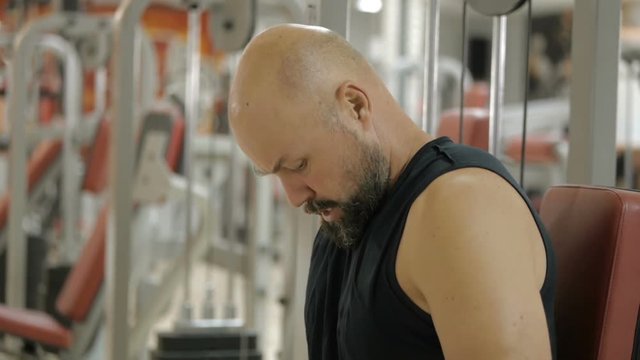 White bold bearded man is doing dips exercise on a machine in gym