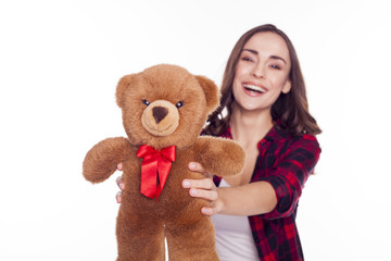 Beautiful smiling young brunette girl with clean skin in a red checkered shirt holding a Teddy bear isolated on white