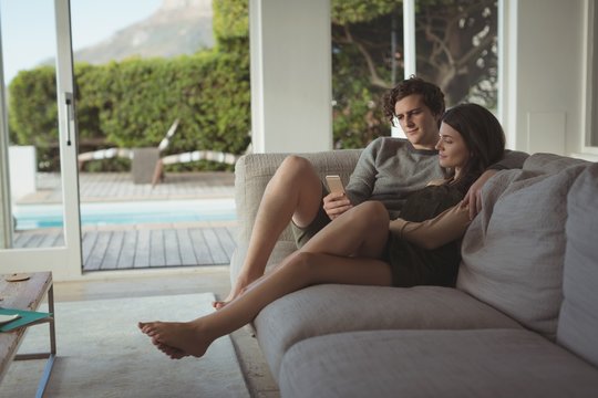 Smiling couple using mobile phone in living room