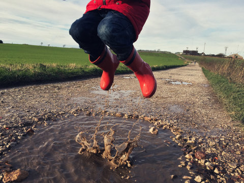 Child jumping in a muddy puddle