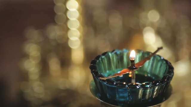 Small wax candle burns on candlestick in temple indoors. Little candle stands on metal candlestick placed in glass bowl in darkened room of ancient Cathedral church. Bright light of small object
