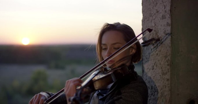 Playing violin in ruined building with sunset 4K.