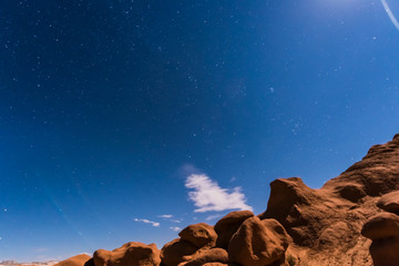 Night sky with full moon rising, or moonrise, in Goblin Valley State Park in Utah showing clouds,...
