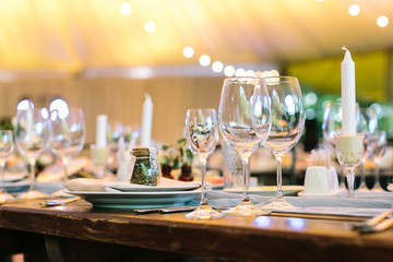 event, table setting, celebration concept. on the table there is plate, silverware, three dazzling glasses, that shining in the lights, and candle in the original holder