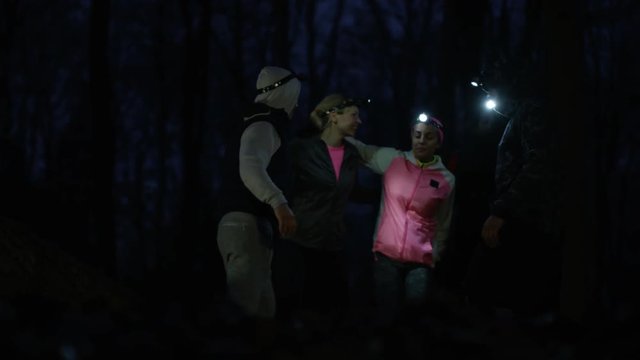 Cheerful group running in the woods at night wearing lamps on headgear.