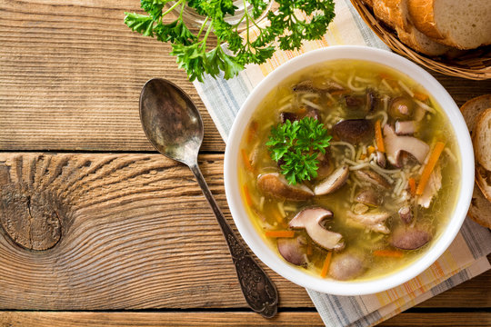 Chicken soup with mushrooms and noodles on rustic wooden table