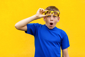 Funny boy in color glasses looking at camera and shocked.