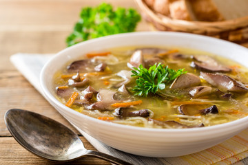 Chicken soup with mushrooms and noodles on rustic wooden table