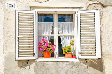 Fototapeta na wymiar Picturesque window , shutters, colorful flowers against a white limestone wall