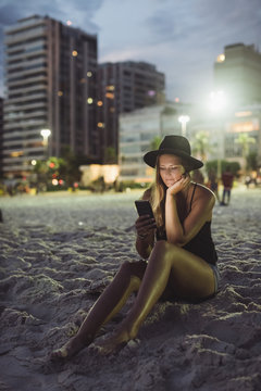 Rio de Janeiro. Brazil. Woman using mobile phone while sitting on the beach at sunset