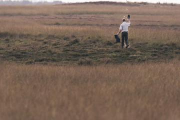 Park ranger scattering food in field with yellow grass.