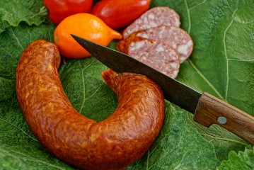 Копчёная колбаса с ножом и спелые помидоры на зелёном...