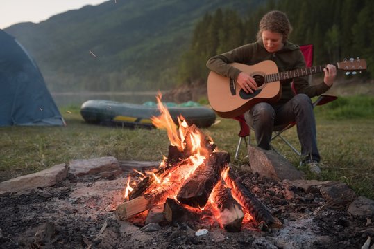 Woman playing guitar near campfire at campsite