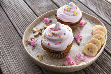 Obraz na płótnie Canvas Two beautiful cupcakes served on wooden table decorated with bananas and small pink flowers