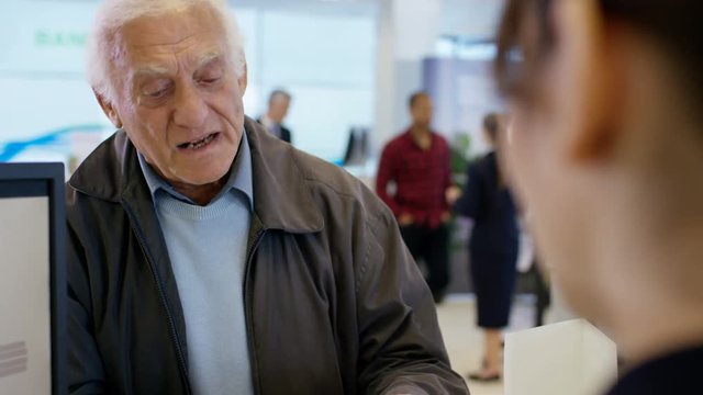  Worker At Customer Service Desk Assisting Senior Customer In Modern Bank