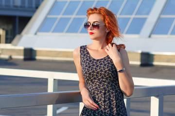 Young beautiful girl with beautiful appearance. Red-haired woman with a pretty face at sunset. A charming, smiling woman portrait  with a beautiful look, posing against the backdrop of the cityscape.