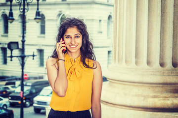 East Indian American Business Woman in New York. Wearing sleeveless orange shirt, a beautiful college student smiling, calling on phone on street, many cars on background. Instagram filtered effect.