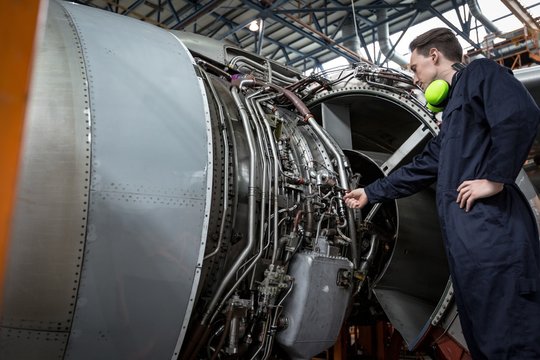 Male aircraft maintenance engineer examining turbine engine of