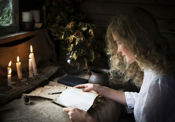 Girl reading a book in the magical mystical ancient dark room with candles