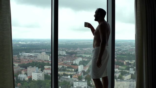 Man in towel drinking coffee and admire view from window, super slow motion 120fps
