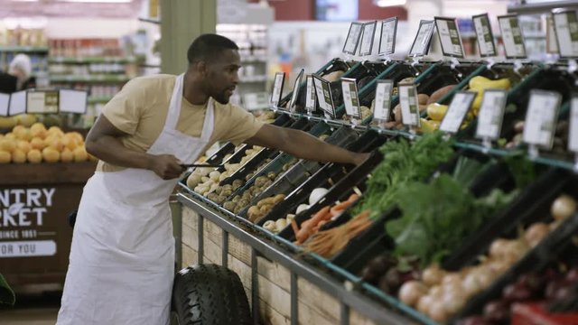  Grocery store worker checking fresh produce & using tablet computer