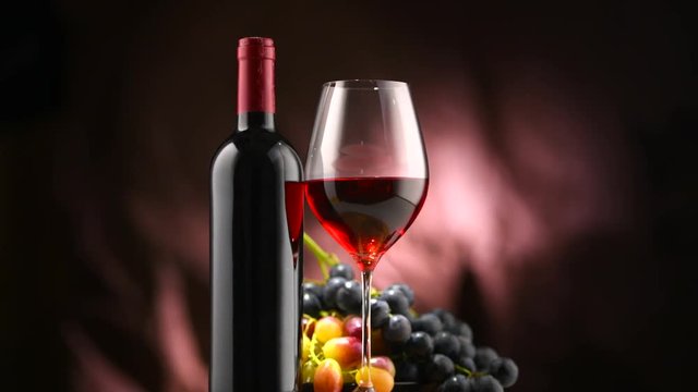 Wine. Bottle and glass of red wine with ripe grapes over black background. Rotation 360 degrees. 4K UHD video footage. Ultra high definition 3840X2160
