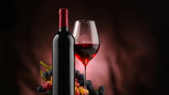Wine. Bottle and glass of red wine with ripe grapes over black background. Rotation 360 degrees. 4K UHD video footage. Ultra high definition 3840X2160